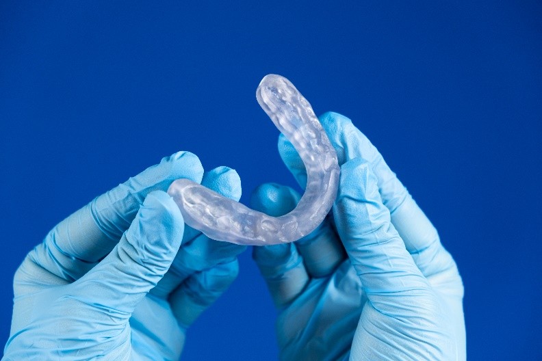 Eine transparente Schiene wird von zwei Händen in Handschuhen gehalten.